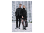 Pár v elegantních černých outfitech pózuje před moderní budovou.