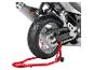Zadní část motocyklu na červeném stojanu, ukazující pneumatiku, řetěz a výfuk