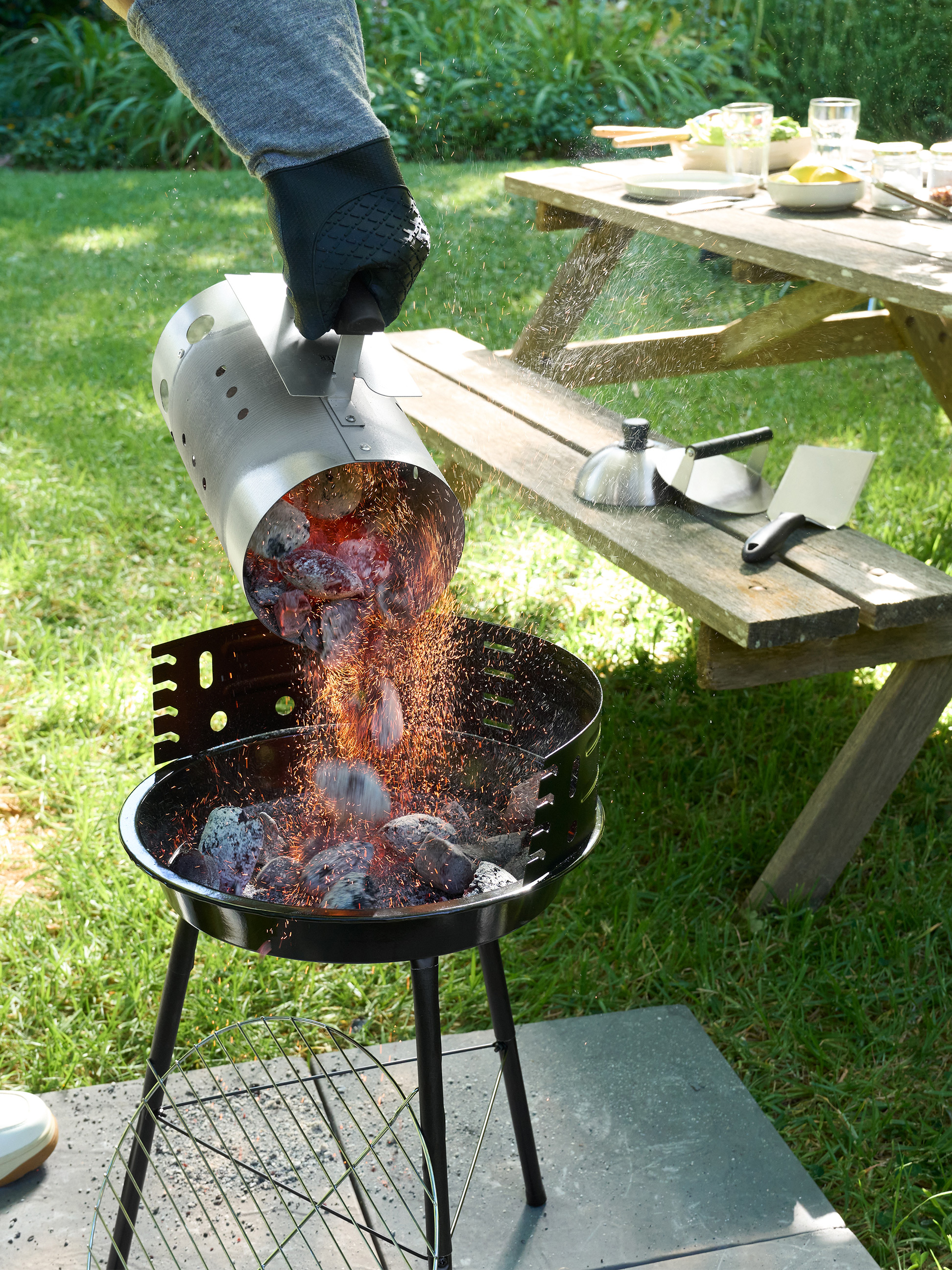 Žhavé uhlíky se sypou z podpalovacího komínu do grilu na dřevěné uhlí na zahradě.