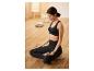 Žena v černém sportovním podprsenku a legínách medituje na polštáři na meditaci.