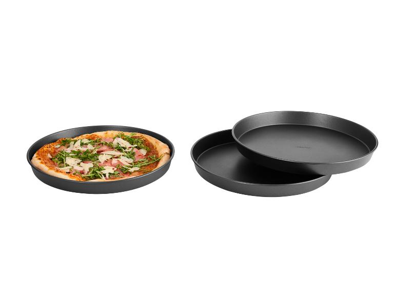 Pizza v kulatém pečicím plechu, se dvěma prázdnými kulatými plechy vedle.