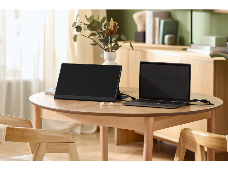 Přenosný monitor a notebook připojené na dřevěném stole ve světlém pokoji.