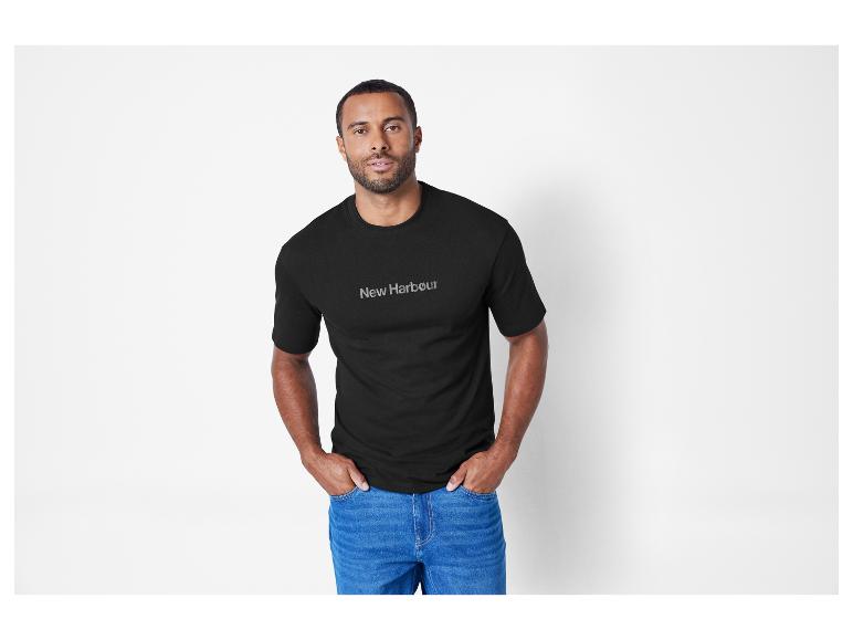 Muž v černém tričku New Harbour a džínách.