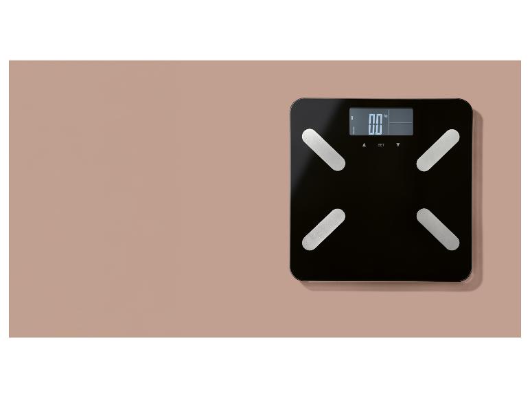 Černá digitální váha s displejem zobrazujícím „0.0 kg“ umístěná na světle růžovém povrchu.