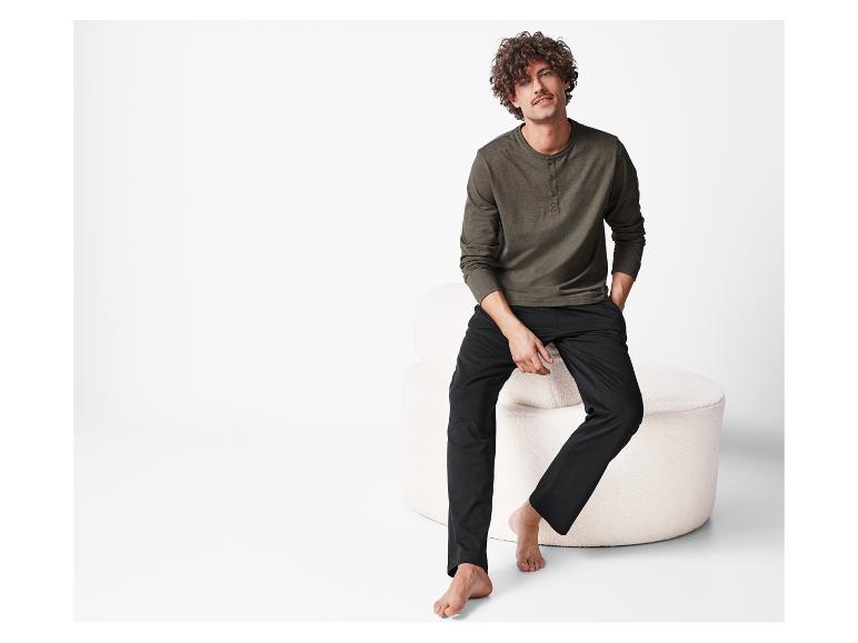 Muž s kudrnatými vlasy pózuje v tmavě zelené a černé pyžamu.