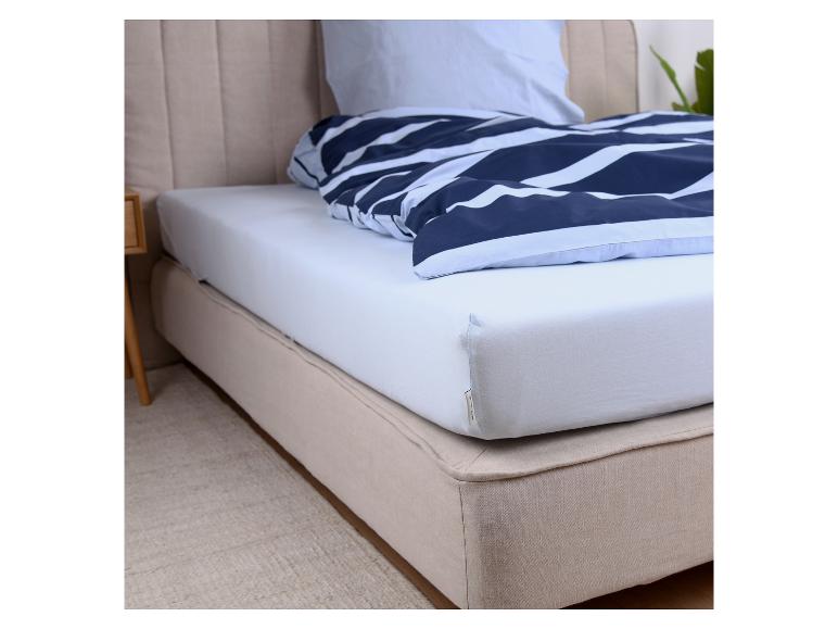 Postel s bílým prostěradlem a modrou pruhovanou peřinou.