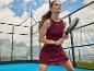 Žena ve sportovních šatech s pálkou na padel na venkovním kurtu.