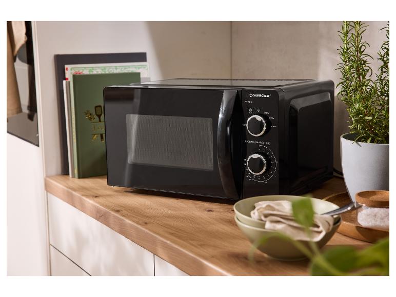 Černá mikrovlnná trouba Silvercrest na dřevěné desce s kuchařkami a rostlinou.