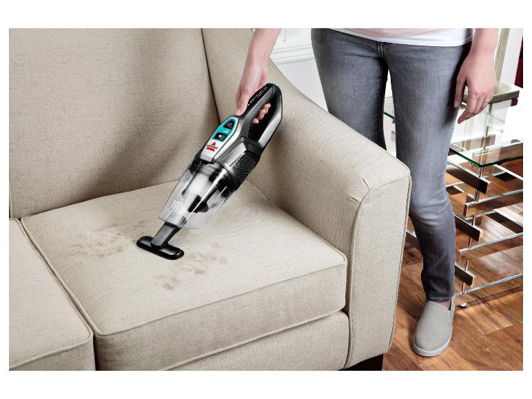 Žena čistí látkovou pohovku ručním vysavačem Bissell