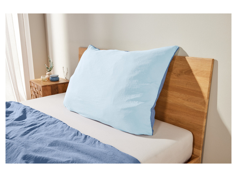 Světle modrý polštář na posteli s tmavě modrou přikrývkou
