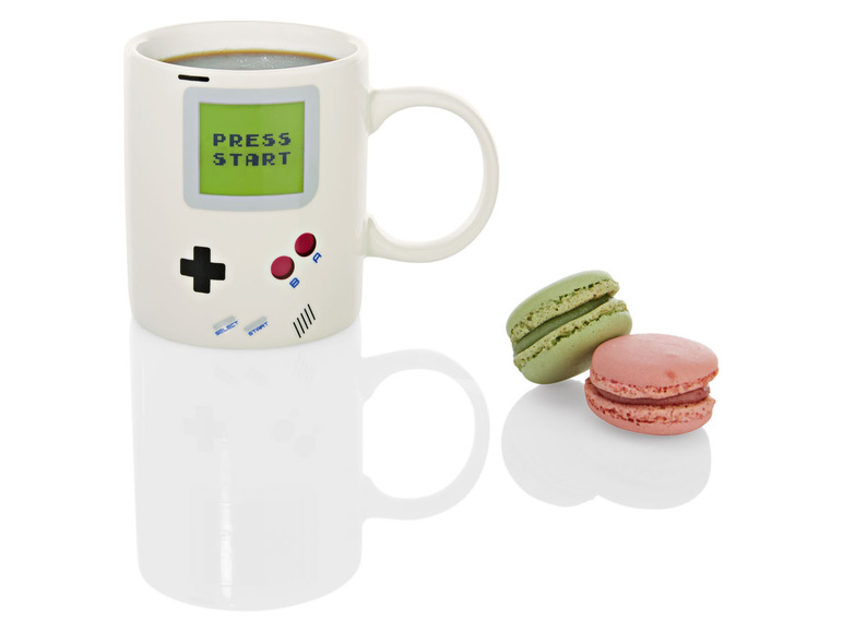 Hrneček s designem Game Boy vedle dvou makronek.