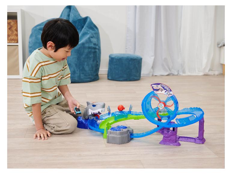 Dítě si hraje s dráhou Hot Wheels Shark Cyclone na dřevěné podlaze.