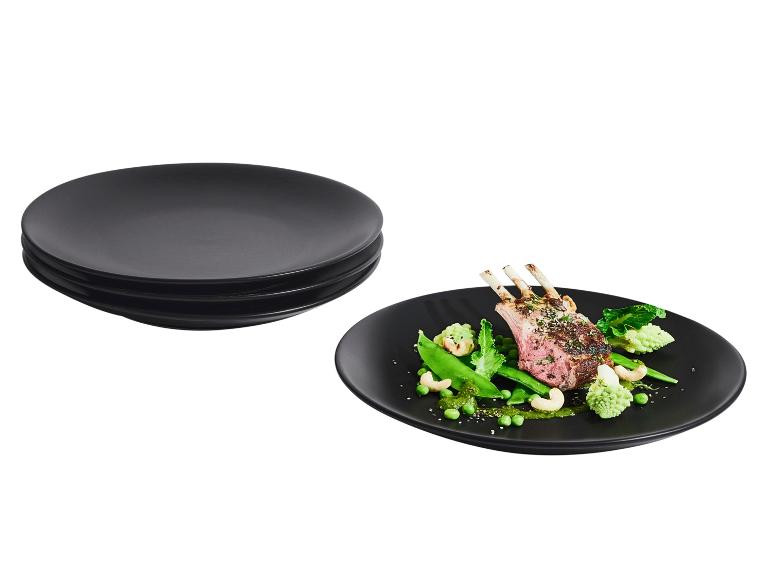 Skládané černé talíře a černý talíř s jehněčími žebírky a zeleninou.
