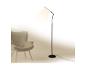 Moderní černá stojací lampa osvětlující šedé křeslo v minimalistickém interiéru.
