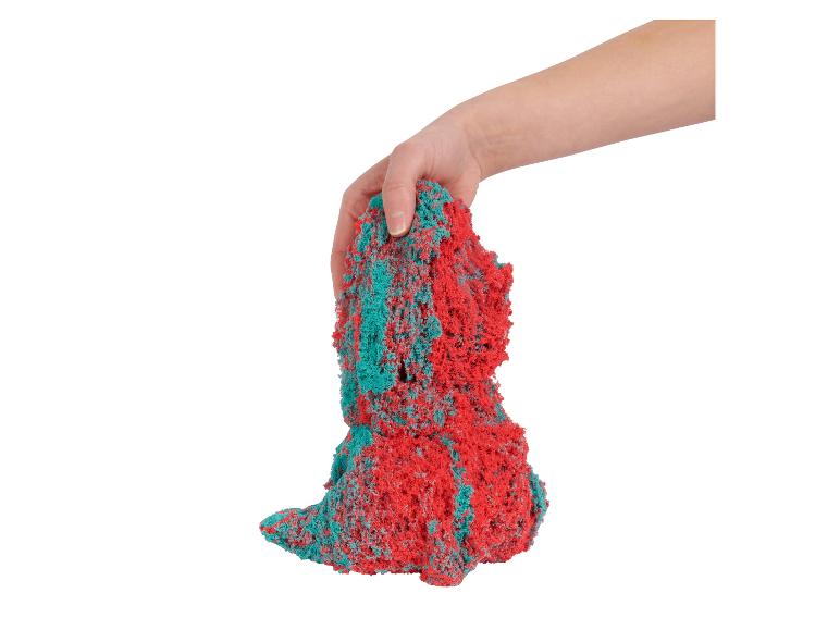 Ruka drží hrudku červeného a tyrkysového kinetického písku.