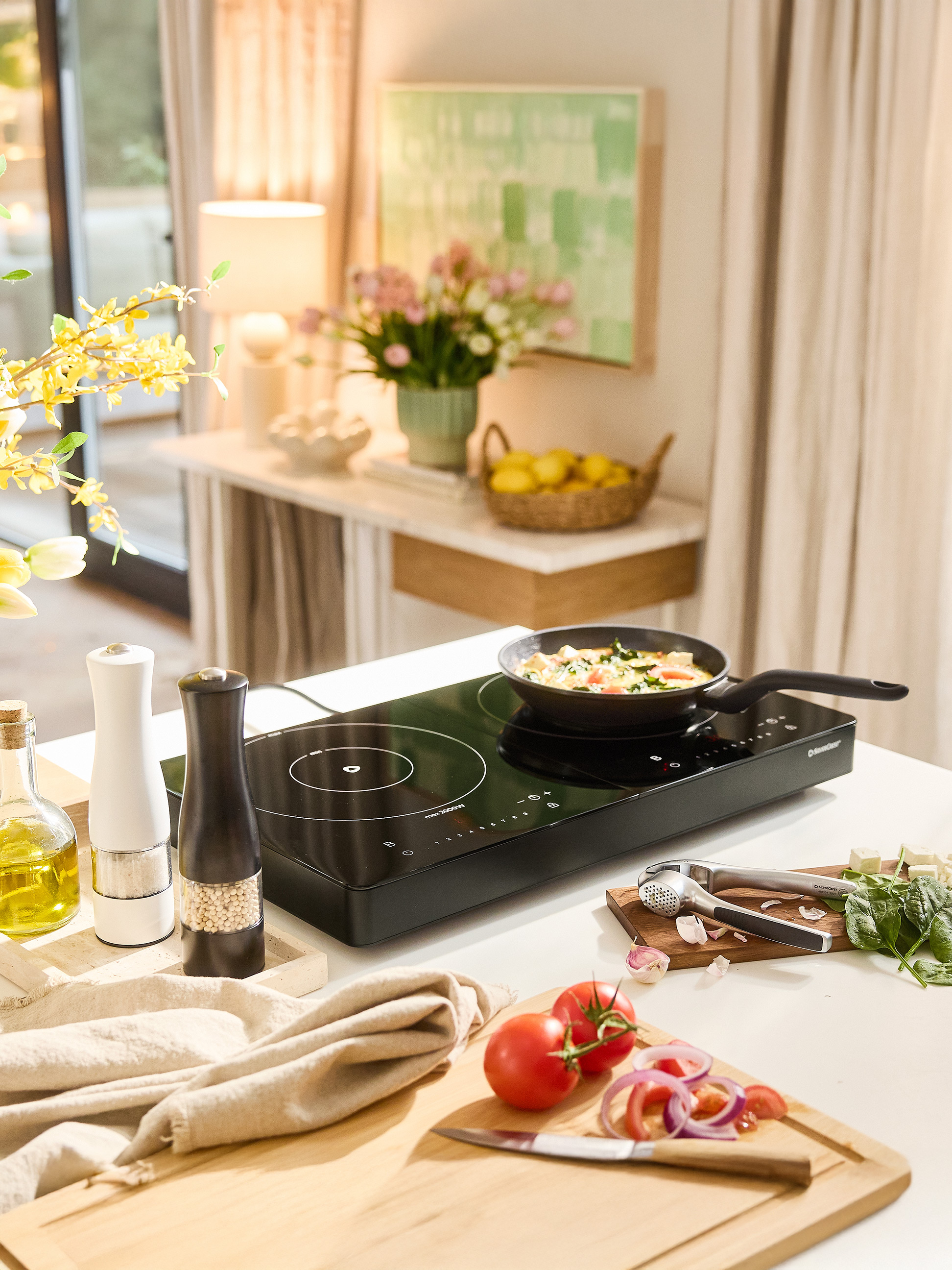 Indukční varná deska SilverCrest s pánví, kořením a čerstvou zeleninou na kuchyňské lince.