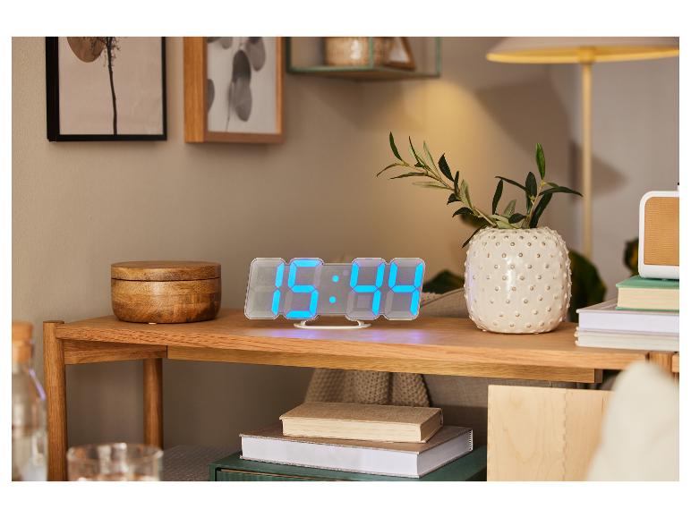 Digitální LED hodiny, knihy a ozdobná váza na dřevěném nábytku.