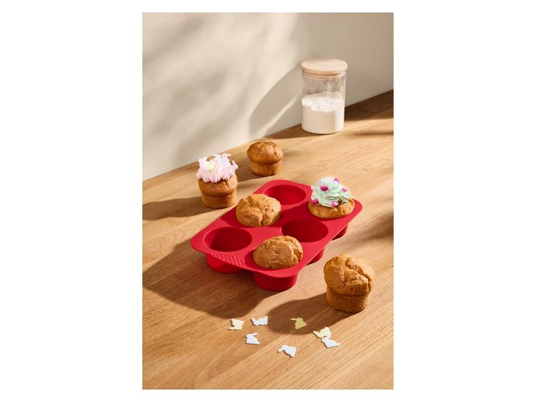 Červená silikonová forma na muffiny s muffiny, některé zdobené polevou.