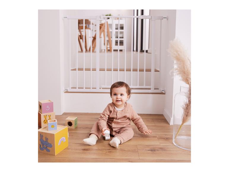 Dítě sedící na dřevěné podlaze s hracími kostkami a bílou bezpečnostní zábranou v pozadí.