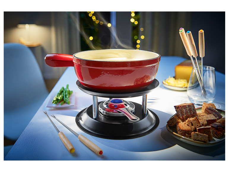 Červený hrnec na sýrovou fondue s vidličkami na fondue a kostkami chleba.