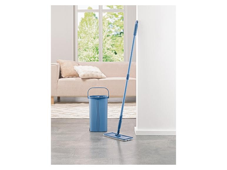 Modrý kbelík a mop ve světlém obývacím pokoji s pohovkou a oknem.