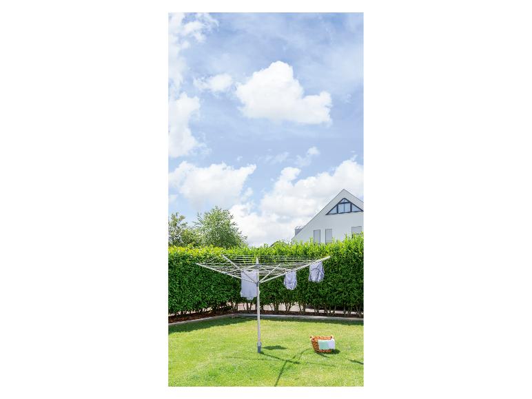 Otočný sušák na prádlo se sušícím se prádlem v slunné zahradě.