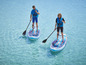 Dva lidé paddleboardují na modrých Red Paddle Co. paddleboardech v tyrkysové vodě.