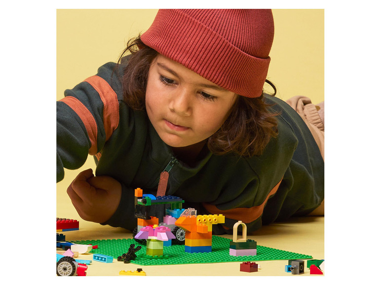 Dítě staví z kostek LEGO, včetně malého auta a květin.