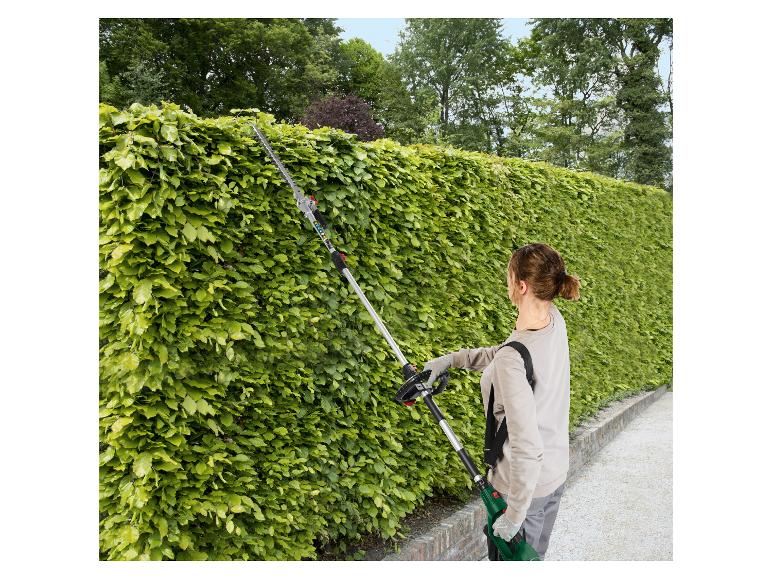 Žena používá dlouhé STIHL nůžky na živý plot k prořezávání vysokého živého plotu.