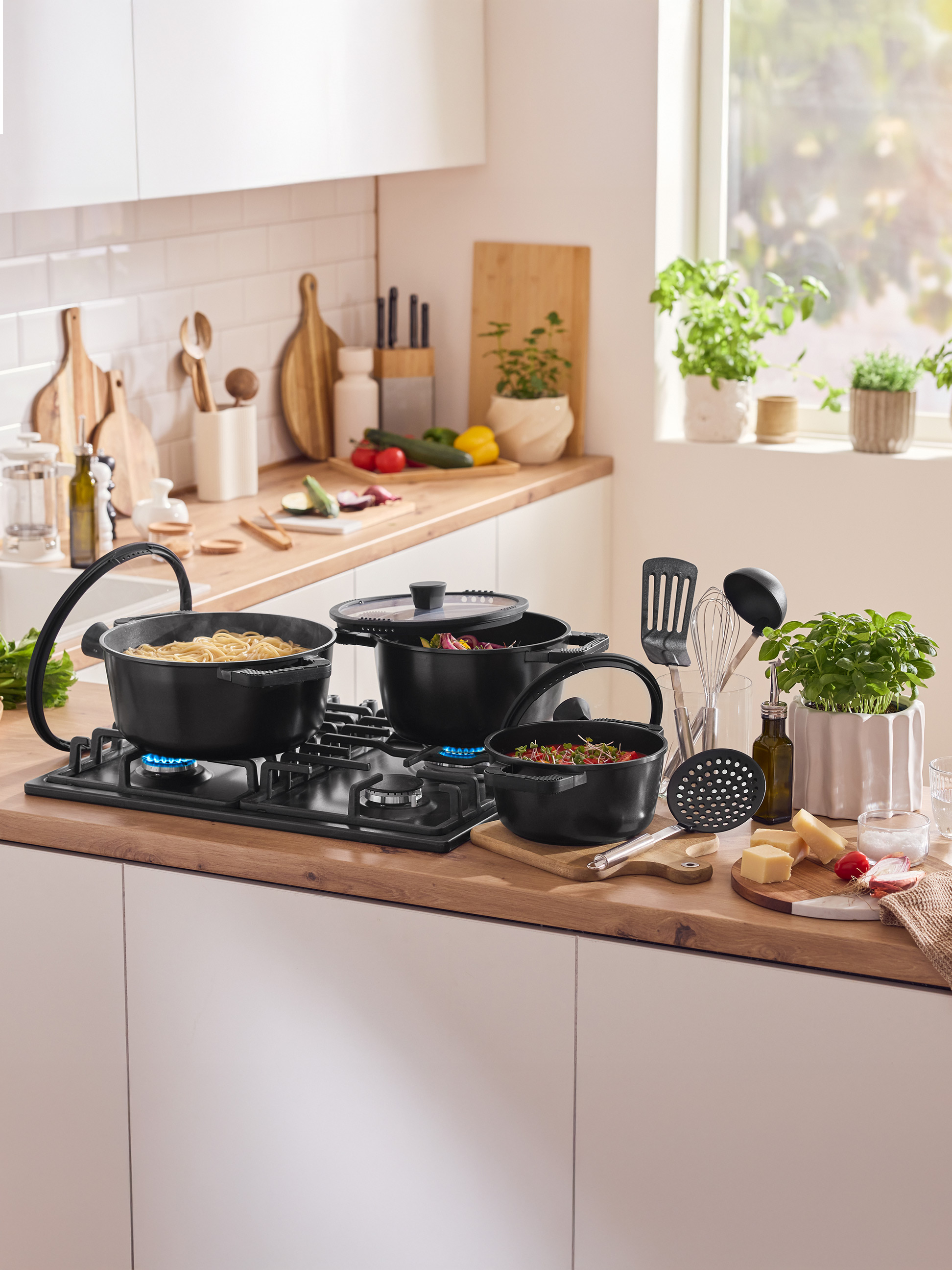 Kuchyňská linka s hrnci na sporáku, kuchyňským náčiním a čerstvými ingrediencemi.