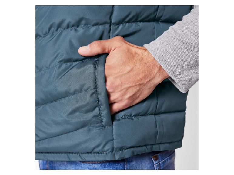 Muž má na sobě tmavě modrou prošívanou vestu s rukou v kapse.