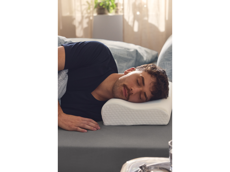 Muž spící na boku na šedém povlečení, s hlavou na ergonomickém polštáři.