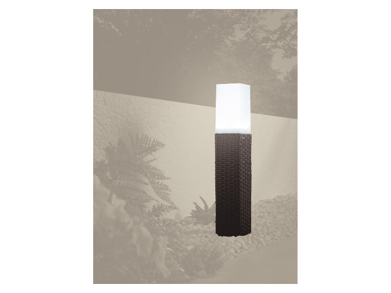 Zahradní lampa ve tvaru pleteného sloupu osvětlující štěrkovou cestu.