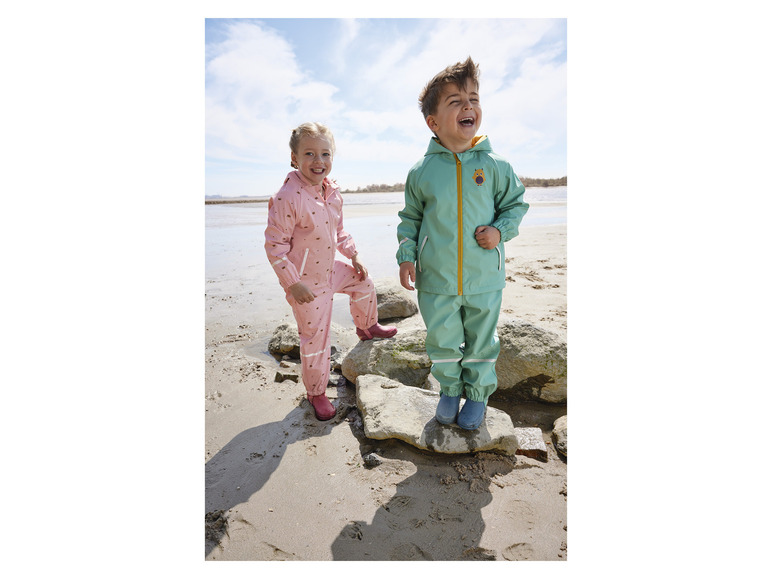 Dvě děti v deštivém oblečení na pláži.