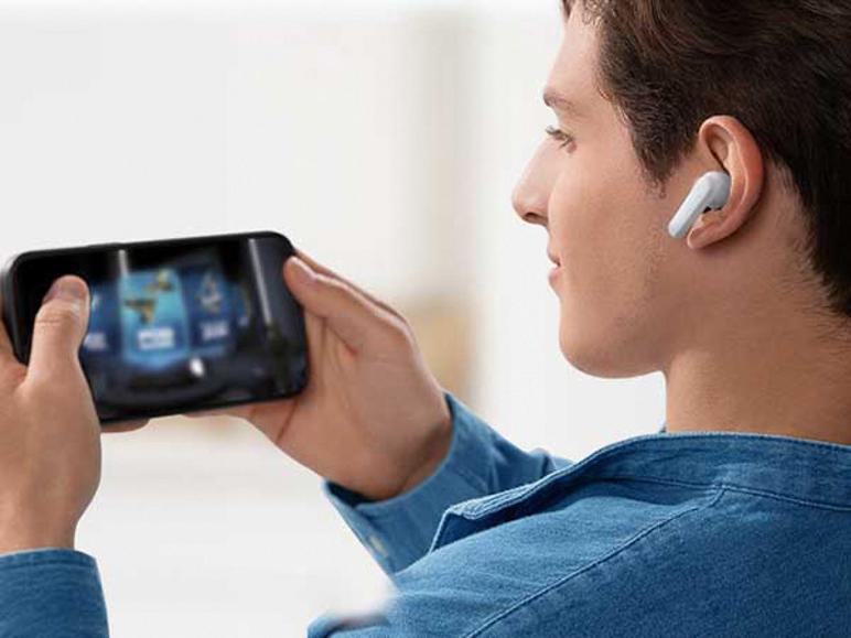 Muž v džínové košili hraje na smartphonu, nosí bílé sluchátko do ucha.