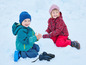 Dvě děti v zimním oblečení si hrají ve sněhu.