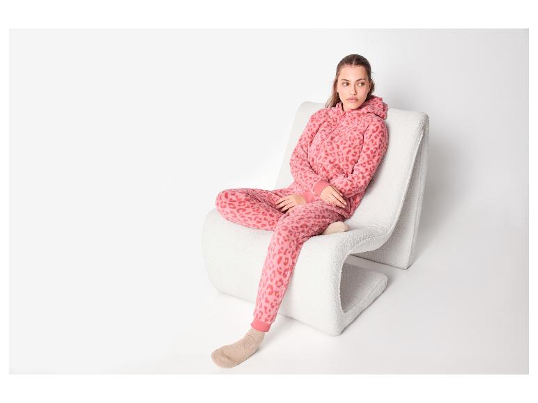 Žena v růžovém pyžamu s leopardím vzorem, sedící na bílé židli.