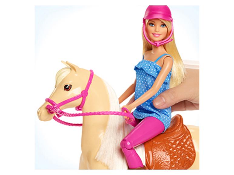 Panenka Barbie jedoucí na hračkovém koni, držená lidskou rukou.