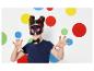 Dívka s kočičí maskou a mašlí před zdí s barevnými puntíky.