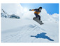 Snowboarder v modré bundě a černé helmě skáče nad sněhem.