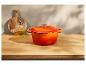 Oranžový litinový hrnec Le Creuset na dřevěné desce.