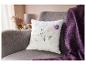 Polštář s květinovým vzorem na šedé pohovce s fialovou dekou.
