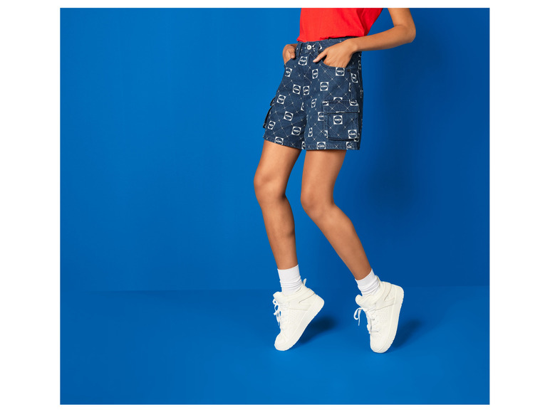 Modelka v džínových šortkách s potiskem Levi's a bílých teniskách.