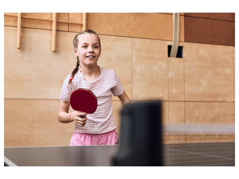 Dívka hraje stolní tenis, drží červenou pálku.