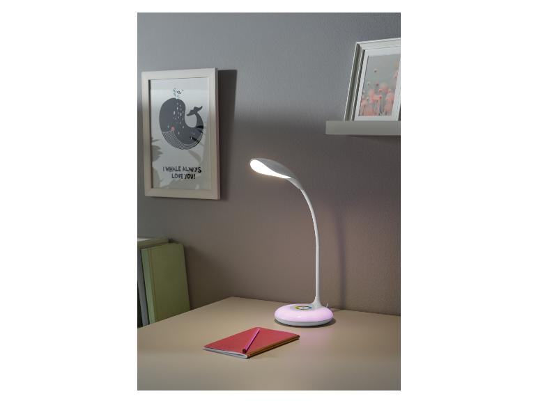 Bílá stolní lampa s barevným světlem, sešit a tužka na stole.