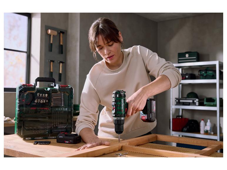 Žena používá akumulátorovou vrtačku k montáži dřevěného rámu, vedle ní je sada bitů.