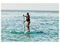 Žena pádluje na paddleboardu v moři, oblečená v záchranné vestě.