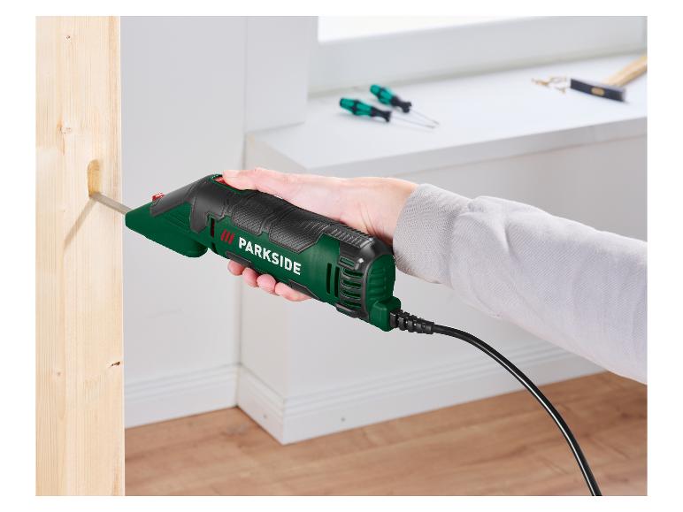 Ruka drží elektrické dláto, které vyřezává otvor do dřevěného trámu.
