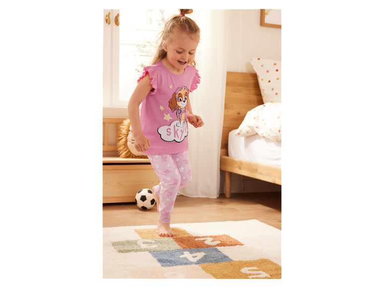 Dívka v pyžamu Paw Patrol si hraje na koberci.