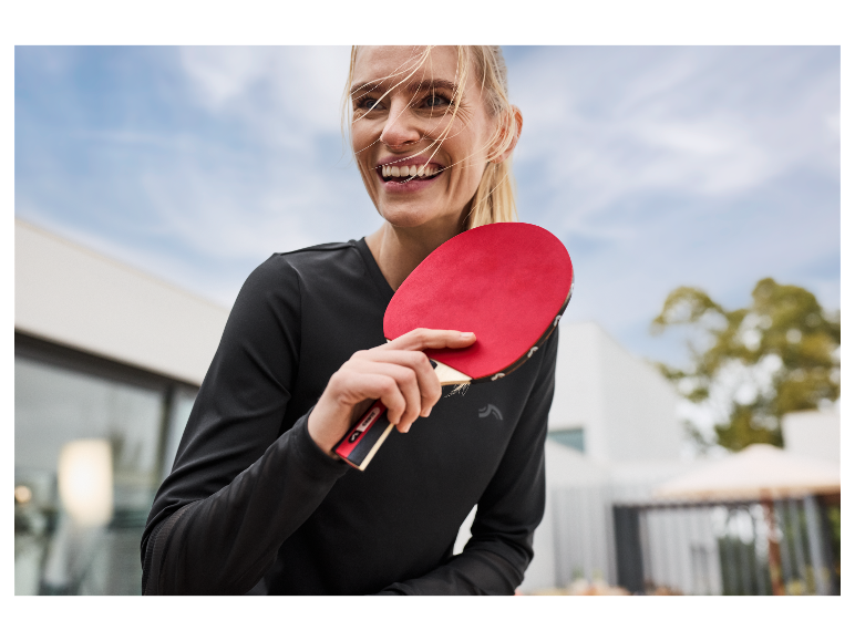 Žena s úsměvem drží červenou raketu na stolní tenis.